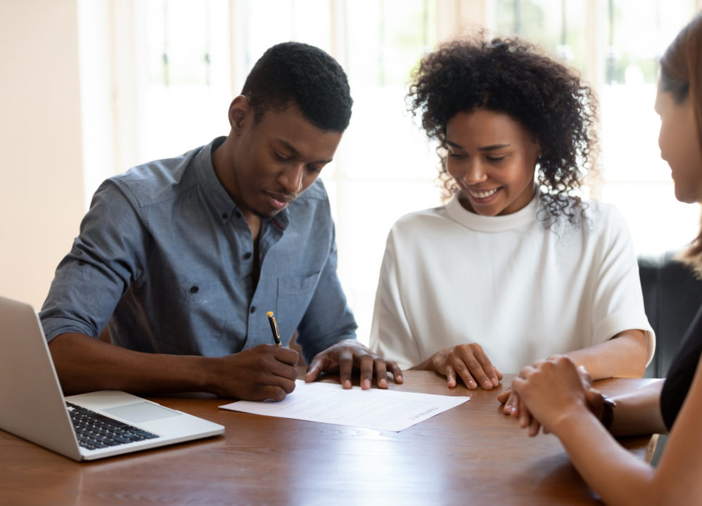 Happy young couple signing financial agreement with agent.