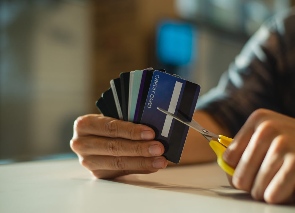 Young man cutting credit card with scissors due to debt.