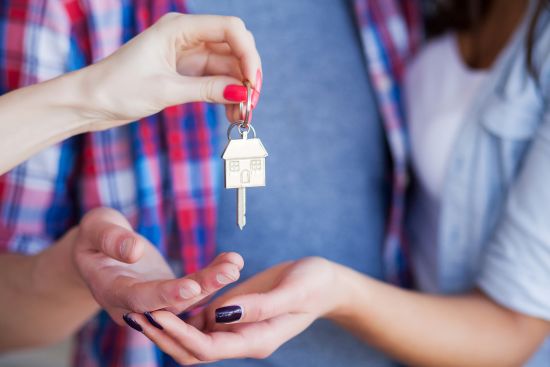 Close-up of a key with a house-shaped keychain being handed over, symbolizing achieving major financial goals like homeownership by selling an annuity.