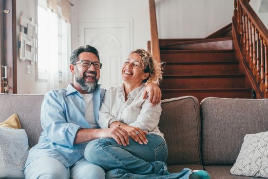 A relaxed couple laughing together on a couch, reflecting the peace of mind achieved after selling annuity payments for quick cash.