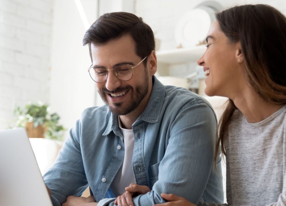A cheerful couple working on a laptop, researching structured settlement buyers at home.