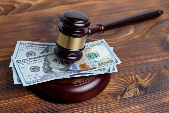 Judge's gavel resting on hundred-dollar bills, symbolizing financial compensation in legal settlements and lawsuits.