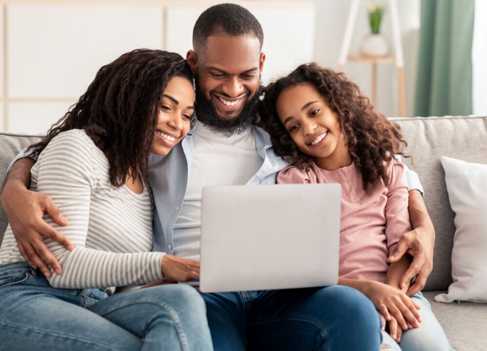 Smiling family using a laptop together at home, exploring financial solutions with DRB Capital for structured settlements and annuity payments.