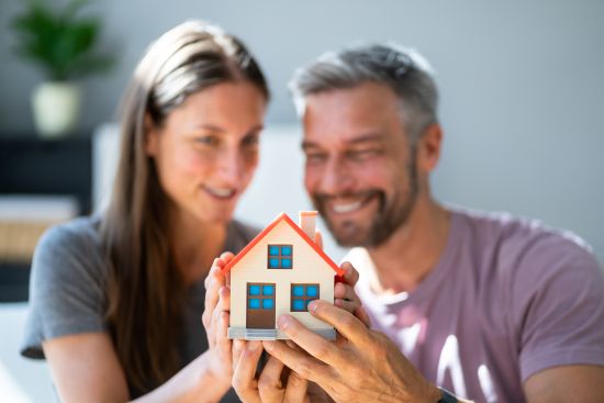 Smiling couple holding a miniature house, considering selling an annuity for a lump sum to pay off their mortgage and achieve homeownership security.