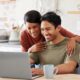 Happy couple using a laptop at home to manage their finances with DRB Capital, experts in structured settlements and annuity payments.