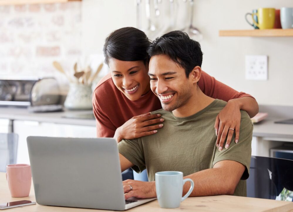 Happy couple using a laptop at home to manage their finances with DRB Capital, experts in structured settlements and annuity payments.
