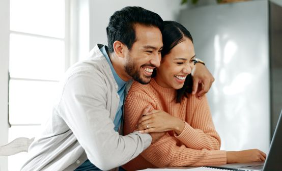 Smiling couple embracing while looking at a laptop, researching how to sell an annuity for financial debt relief.