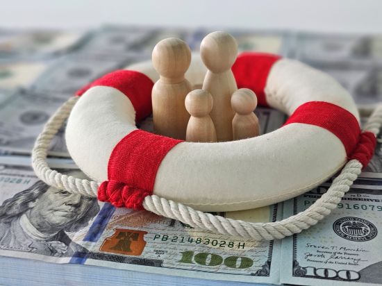 Wooden figurine family surrounded by a life preserver on a pile of cash, symbolizing financial security and annuity lump sum options.