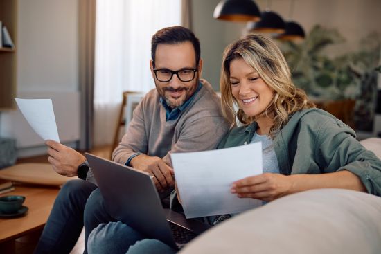Smiling couple reviewing financial documents on a laptop, considering selling their structured settlement payments to get out of debt.