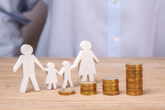 Wooden family cutouts with stacked coins symbolizing financial planning and lump sum settlement benefits.