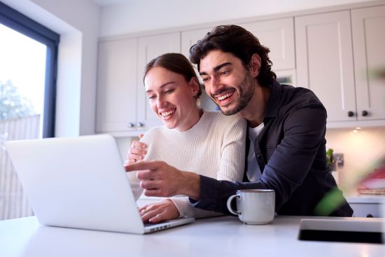Couple smiling at laptop in bright kitchen while learning the steps to sell structured settlement for immediate cash