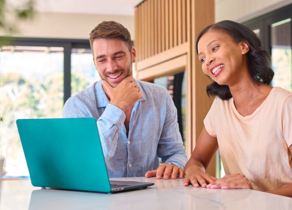 Smiling couple looking at laptop together in bright kitchen while learning what are structured settlements