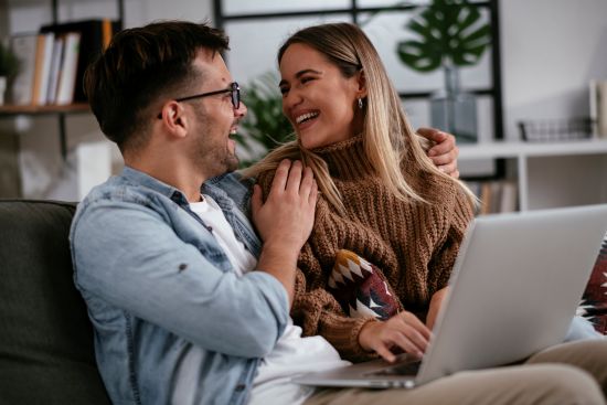 Couple smiling while reviewing options to sell their structured settlement on a laptop at home.