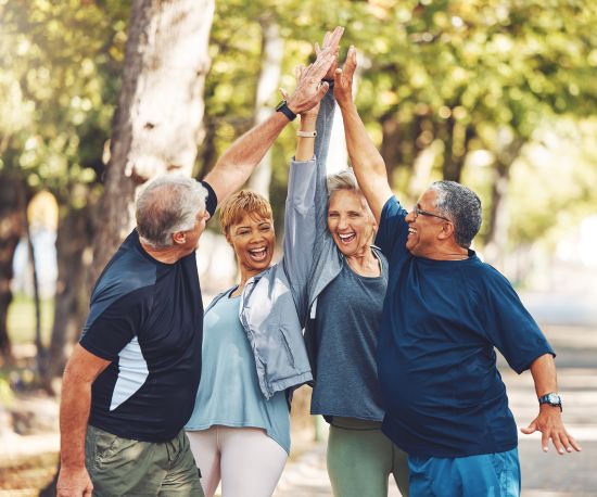 Group of older adults smiling and giving a high-five while exercising together outside.