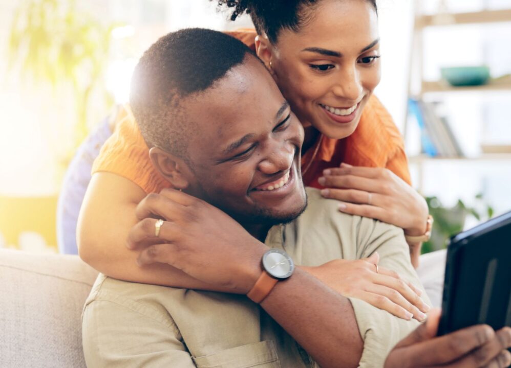 Couple celebrating good news while reviewing financial information on a tablet.