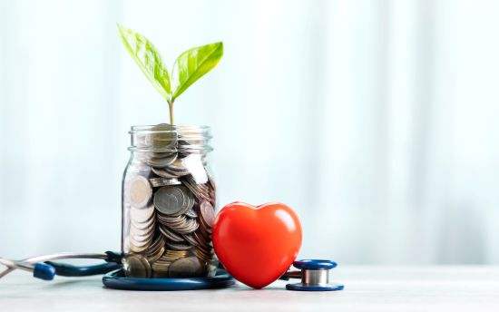 Jar filled with coins and a small plant sprout beside a heart-shaped object and stethoscope, symbolizing financial and personal wellness.